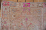 Hand-knotted distressed Oushak rug, showing fuchsia floral motifs, beige pile, and visible wear.