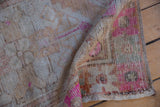 Distressed vintage Oushak rug showing worn texture, fuchsia floral patterns, and beige tones.