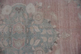 Distressed Oushak rug close-up: visible wear and faded seafoam green blossoms on dusty rose field.