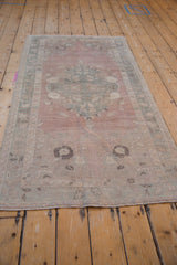 Muted dusty rose and seafoam green blossoms on the distressed vintage Oushak rug's center medallion.