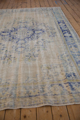 Angled view of a distressed Oushak carpet showing its textured low pile and blue floral border.