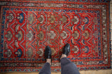Vintage Hamadan rug with person's feet on its tomato red field and geometric floral pattern.