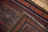 Beshir rug corner: deep red, indigo geometric patterns, exposed foundation, and worn fringe.