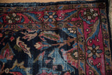 Vintage Lilihan rug corner detail, navy and raspberry floral border, visible pile wear, tattered edge.