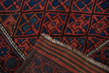 Vintage Belouch rug, folded, displaying madder red, sapphire blue diamond lattice, pomegranate border, and striped back.