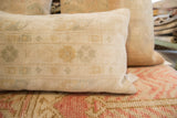 Textured side of a hand-knotted vintage rug fragment pillow, showing softened ivory and pale green motifs.
