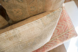 Side detail of vintage rug fragment pillow, showing hand-knotted texture with beige pile and tan piping.