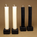 Two cream and two black beeswax column taper candles on dark square bases.