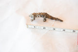 Small bronze pangolin casting measured with a tape to show its four-inch length.