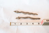 Two vintage bronze snake castings with different patterns measured against a ruler for scale.