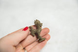 Vintage rooster pendant with dark bronze patina held to show its small scale.