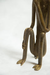 Detailed view of the cast bronze monkey's slender legs and hand resting on a knee.
