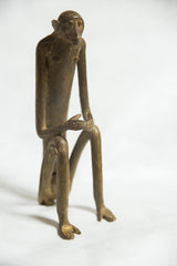 The aged bronze patina on the elongated torso and face of a seated monkey.