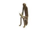 Vintage African bronze sculpture of a seated monkey with long, slender limbs peeling a banana.
