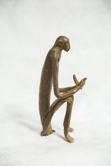 Profile of the seated monkey bronze figure, showing its long, slender limbs and body.