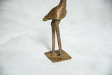 The slender cast bronze legs and textured square base of the vintage bird sculpture.