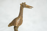 Detail of the vintage bronze bird sculpture's head, featuring the triple horn and circular eye.