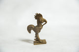 Profile of a stylized bronze rooster sculpture with textured coil patterns and a fanned tail.
