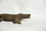 Close profile view of the cast bronze crocodile's head showing its imperfect, broken snout.