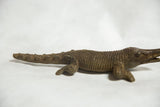 Profile view of the cast bronze crocodile showing its ribbed body and scaly tail.