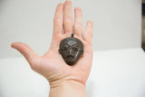 Close-up of vintage African bronze face pendant, intricate features and aged bronze patina in hand.