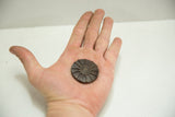 Vintage African bronze coin with a spoked design held in a palm to show scale.