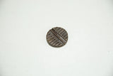 Round African bronze coin with a dark patina and an incised linear pattern.