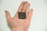 Vintage African bronze coin with geometric pattern, held in hand, showing rich patina.