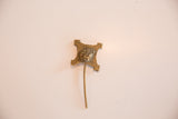 The crafted, four-pointed head of a vintage bronze pin showing its aged, textured patina.