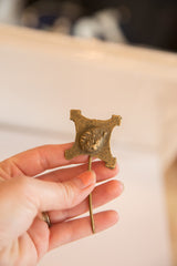 A hand holding the vintage bronze pin, showing its textured, aged patina.