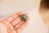 Small bronze African frog pendant held in a hand, showing its scale and vintage patina.
