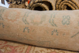 Textured hand-knotted vintage Oushak rug fragment with muted peach and teal geometric motifs.