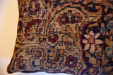 Vintage Kerman rug fragment pillow close-up, revealing worn pile, muted floral pattern, and visible foundation.