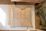 Softly faded hand-knotted vintage rug fragment pillow with peach, beige, and faint blue motifs.
