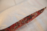 Angled side of antique 1920s Malayer rug fragment pillow, featuring muted red and blue patterns.
