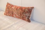 Textured surface of antique 1920s Malayer rug fragment pillow in faded reds and neutrals.
