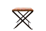 Rug fragment footstool with time-softened red, orange, and muted geometric patterns on a dark industrial base.