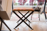 Upholstered vintage rug fragment top in earthy colors on a dark industrial X-frame base.