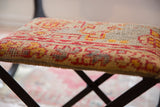 Textured vintage rug fragment footstool with a geometric pattern in reds, golds, and beige.