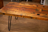 Reclaimed wood coffee table top shows varied grain, embedded bolts, and surface holes.