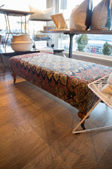 Antique Persian rug fragment ottoman displaying vibrant patterned side, curved wooden legs, and brass casters.