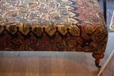 Corner detail of Antique Persian Rug Ottoman, showcasing intricate Khorassan Doroksh pattern and curved wooden leg.