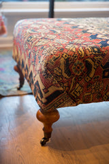 Curved wooden leg and brass caster wheel on antique Persian rug coffee table.