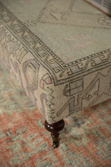 Oushak rug ottoman corner showing light gray geometric pattern, blue dye spots, mahogany leg.