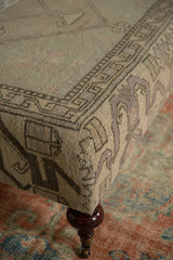 Ottoman corner with gray and light purple geometric Oushak rug pattern, atop a dark wood leg.