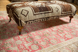 Vintage Oushak rug ottoman with brown and ivory geometric pattern, curved wooden legs.