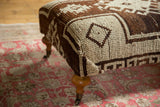 Curved wooden leg with brass caster on the brown and ivory Oushak ottoman.