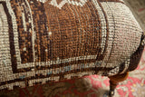 Vintage Oushak rug fragment texture, brown, charcoal, ivory, subtle blue. Ottoman leg with caster.