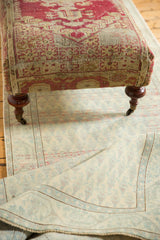 Faded raspberry and ivory antique rug fragment upholstery detail on ottoman with mahogany leg.