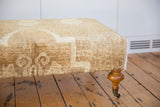 Sheen of vintage Oushak rug ottoman, cream and brown curvilinear pattern, wooden leg.